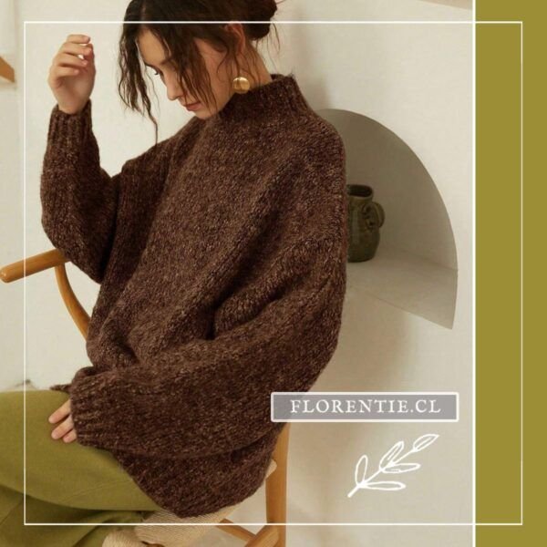 Modelo sentada en silla de madera luciendo chaleco oversize café chocolate con cuello tortuga y mangas voluminosas de punto grueso esponjoso, combinado con falda verde oliva.