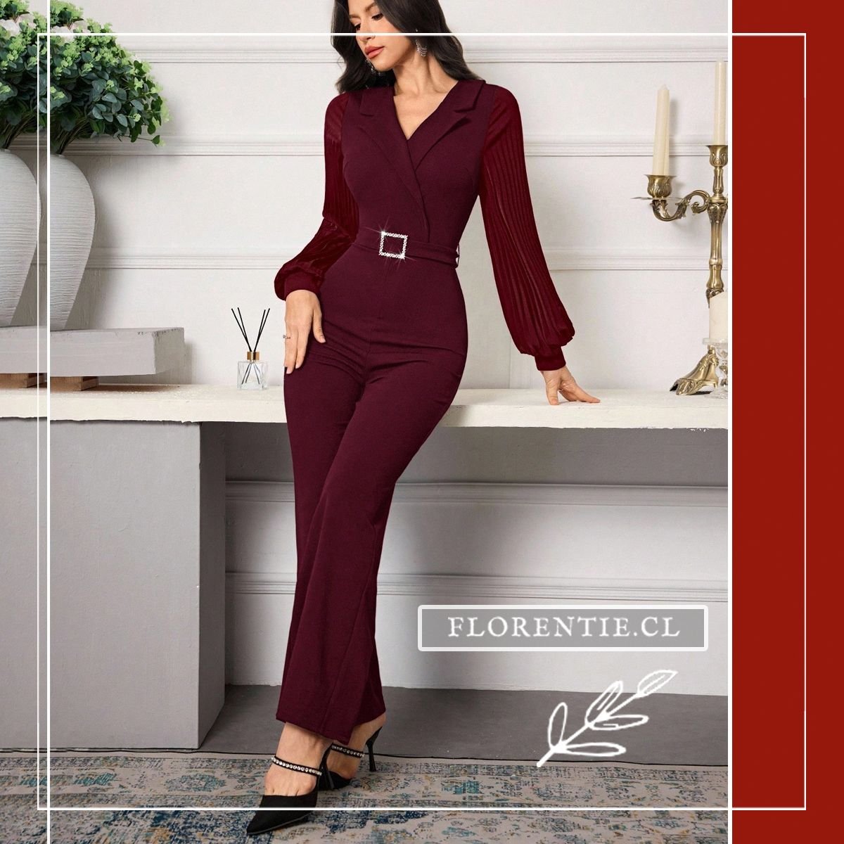 Mujer con mono enterito burdeo de corte recto estilo traje, mangas plisadas largas y hebilla joya, posando junto a consola decorativa