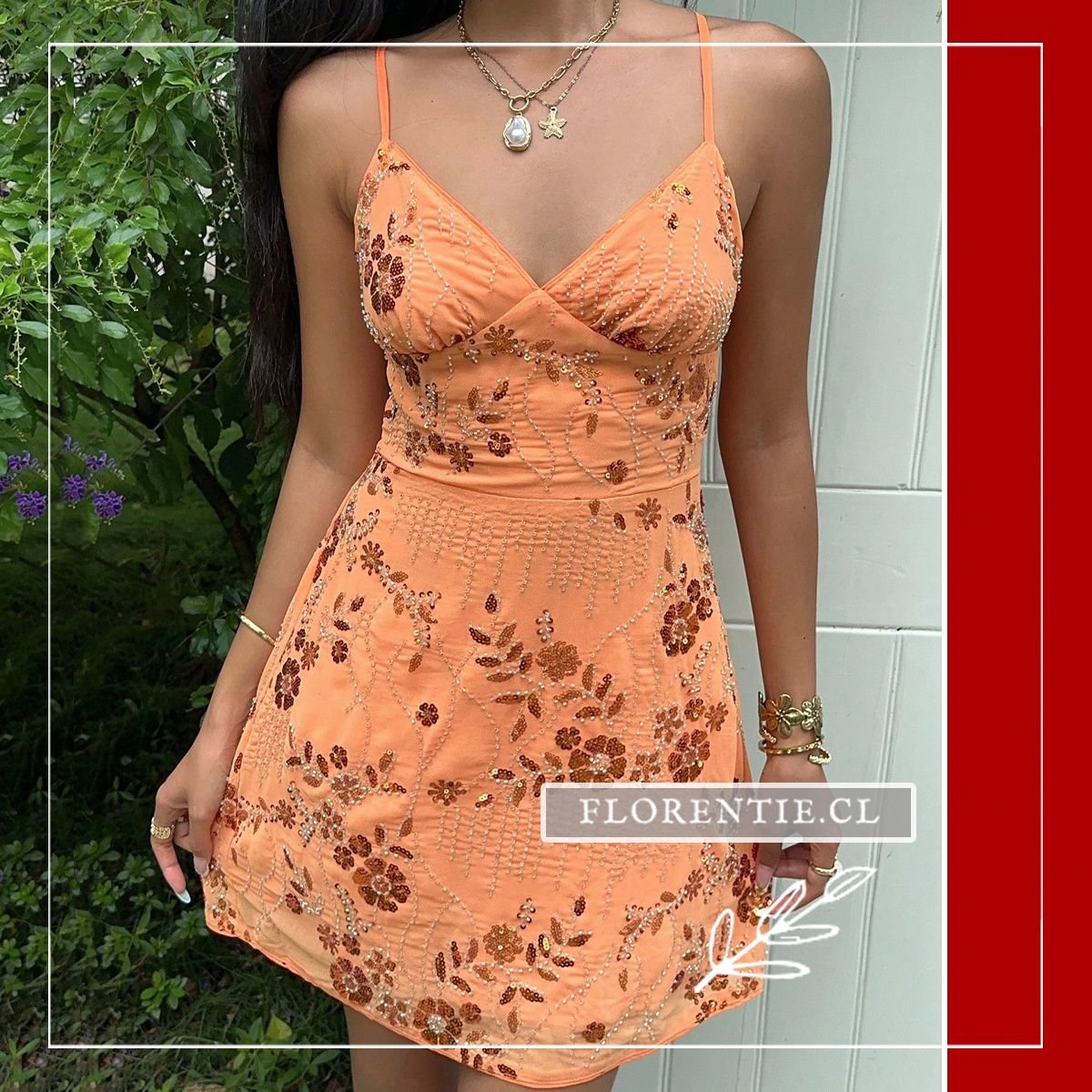 Close-up frontal del vestido mini naranja vibrante con bordado botánico en lentejuelas doradas y pedrería, escote en V con copas estructuradas, combinado con collares dorados en capas.