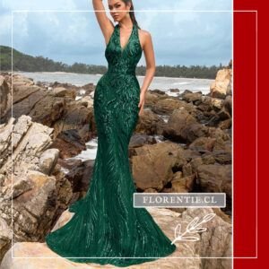 Vista frontal completa del vestido de lentejuelas verde esmeralda con silueta sirena, patrón de ondas orgánicas bordadas, escote halter en V profunda y cola de arrastre, posando sobre rocas costeras.